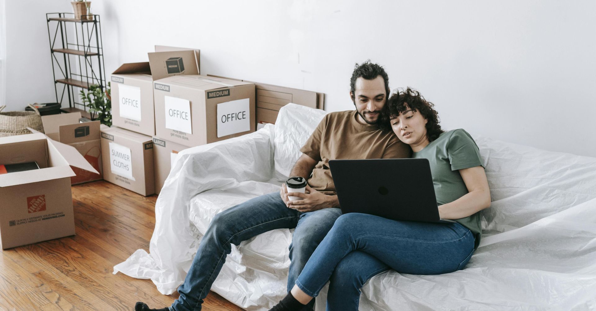 A couple sits together on a couch, using a laptop amidst moving boxes, enjoying relaxed time indoors.